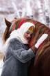 Russian beauty girl in traditional clothes hugging a red big horse in forest winter
