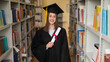 © Михаил Решетников - Happy young woman in graduate gown holding diploma in the library.
