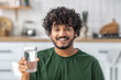 © kucherav - Young Asian man holding a glass of clean fresh water looking at the camera and smiling standing at home