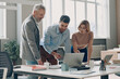 © gstockstudio - Three confident business people having discussion while standing near the office desk together