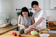 Asian couple in love relationship making a healthy salad together in the kitchen. Smiling happy boyfriend and girlfriend enjoying cooking activity at home apartment.