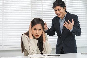 Angry boss, stressed asian young business, employee, secretary woman sitting at desk, hand cover her ears feel upset from annoying boss, colleague conflict with manager mistake about job at office.