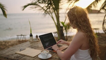 Female developer working on laptop creating apps by the ocean. Young woman freelancer coding at outdoor tropical cafe. Caucasian girl working remotely at exotic location. Worldwide work concept