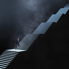 Business Development, Long Career Way And Faith Concept With Woman In Dark Suit Climbs Dark Stairs Illuminated From Above On Abstract Dark Foggy Background