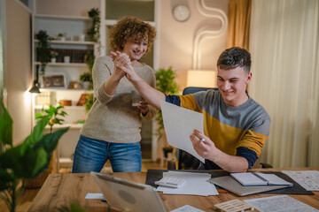 Young man and his mother woman hold paper read good news in letter sit at desk at home beautiful female received correspondence bank statement or notification invitation scholarship pleasant message