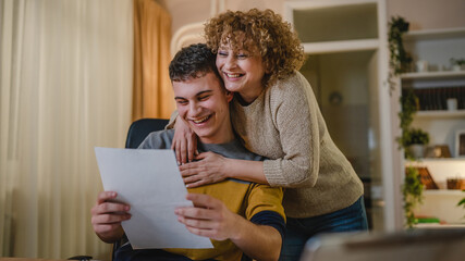 young man and his mother woman hold paper read good news in letter sit at desk at home beautiful fem