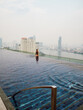 Caucasian woman is sitting at an infinity pool on a rooftop in Bangkok, Thailand