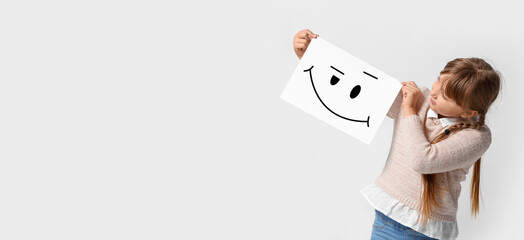 Poster - Little girl holding paper with smiling emoticon on light background with space for text