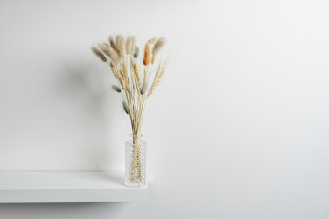 Small carved glass vase with spikes and dried plant branches, some stained on a white wooden shelf and plain white wall