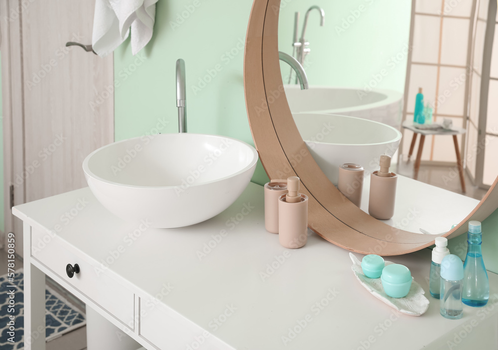Interior of bathroom with ceramic sink and bath accessories near mirror
