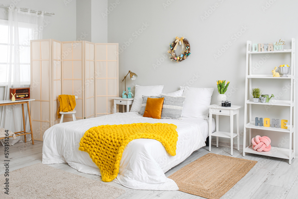 Interior of light bedroom with Easter wreath and tulips in vase