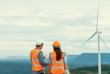 Wall Mural - Male and female engineers working on a wind farm atop a hill or mountain in the rural. Progressive ideal for the future production of renewable, sustainable energy.