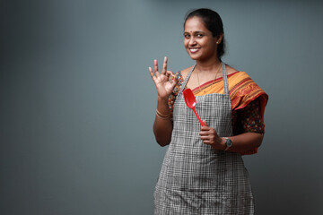 Indian ethic woman wearing apron and holding spatula showing a like gesture