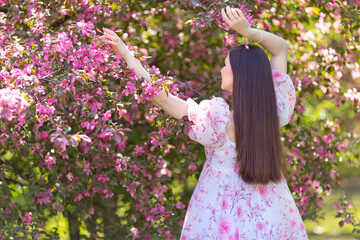 rear view, girl in a pink dress standing near pink blooming tree