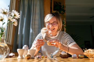 Smiling woman preparing easter decoration at home, painting colorful easter eggs and coloring egg cups.