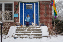 A Small Child Stands In The Falling Snow On Her Front Stoop With Cat