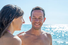Young Couple Standing On Beach While Smiling Against Blue Sky