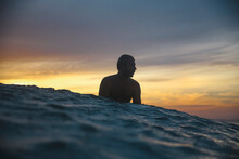 Man Sitting On Surfboard In Sea During Sunset
