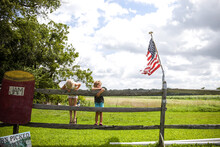 Sisters Hanging On Wooden Fence In Countryside With American Flag