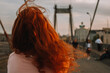 © Cavan Images - Rear view of woman with red hair walking on bridge in city