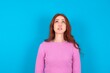 © Roquillo - young woman wearing pink sweater over blue background looking up as he sees something strange.