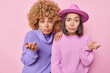 © wayhome.studio  - Two hesitant women shrug shoulders look confused cant make choice stand closely to each other dressed in knitted jumpers isolated over pink wall. Clueless female models stand puzzled feel indifferent