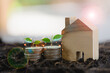 Money growing in soil with houses and plants are growing on coins. Two coins stacked on soil and tree on top for saving money, energy, and income for your family on bokeh background.