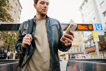 Young man using mobile phone while standing on escalator outdoors