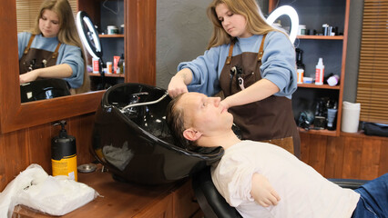 A hairdresser girl washes the hair of a man with limited opportunities in a beauty salon