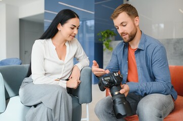 Young photographer man in blue shirt watching photo with client woman after photo session and smiling and looking at each other