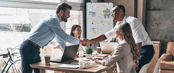 Sticker - Two young men shaking hands while having meetings with colleagues in the office