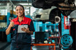 © anon - Engineer team checking under car condition on lifter in garage.Young auto mechanic in uniform is looking at camera and smiling examining car...