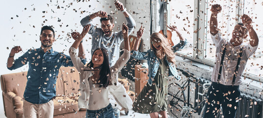 Canvas Print - Beautiful young people dancing together and throwing confetti while having party at home