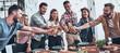 © gstockstudio - Group of young people toasting with beer and smiling while standing near the dining table