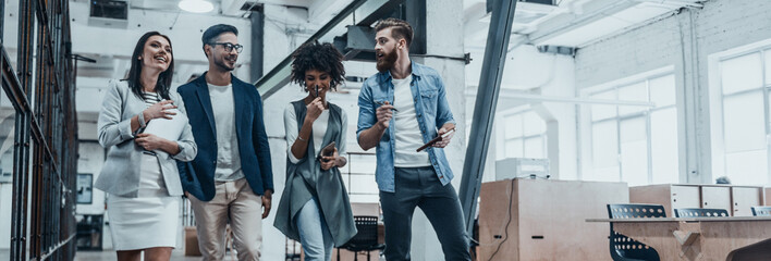 Canvas Print - Group of happy young people discussing business while walking by the office corridor