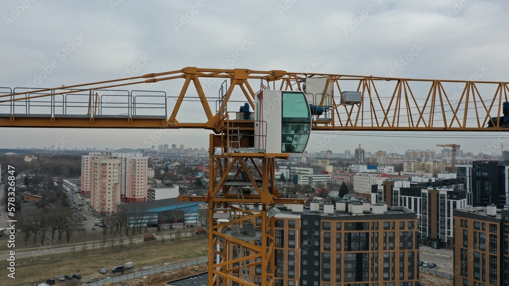 The cab (booth) of the crane operator and the boom of the tower crane close from a height, taken with a quadrocopter. A crane operator sits in the cab of a high-rise skyscraper crane