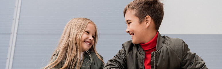 happy preteen kids in bomber jackets looking at each other while standing near mall, banner.