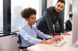© sutthichai - Happy African business woman in wheelchair working with Asian Manager at her desk with computer in the office .