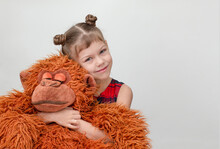 Happy And Smiling Child Hugging Monkey Toy On White Background Caucasian Little Girl Kid Of 6 7 Years In Red Plaid Dress Looking At Camera