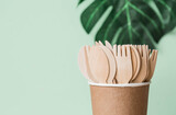 Fototapeta  - Eco-friendly disposable kitchen utensils in a paper cup on a beige-green background. Wooden forks, spoons and knives. Ecology, the concept of zero waste.