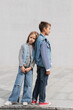 © LIGHTFIELD STUDIOS - full length of well dressed girl in denim outfit leaning on back of boy while standing outdoors.