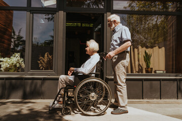 Wall Mural - Senior couple, husband takes care of invalid wife on wheel chair