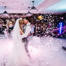 First Wedding Dance Of Newlywed. Happy Bride And Groom Dancing Under Confetti In The Elegant Restaurant With A Wonderful Light And Atmosphere. Romantic Moments.