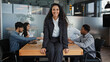 © Yuliia - Satisfied smiling Hispanic businesswoman manager worker woman sitting on table in boardroom office background of multiracial employees coworkers colleagues discuss work business project brainstorming