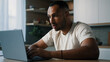 © Yuliia - African ethnic male man at kitchen at home play online game bet losing betting bad result feel frustrated upset working problems business failure with laptop cryptocurrency crash mistake with computer