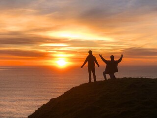 Silhouette of two men on hill raising hands with sunset