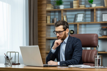 thinking businessman working sitting at desk, mature adult boss in business suit and beard looking a