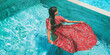 © Maridav - Summer dress fashion model woman swimming in pool wearing long floral red maxi dress clothing. Creative artistic fashion photo shoot at luxury resort infinity pool