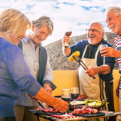 Wall Mural - Happy group of elderly senior people couples eating bbq grill all together having fun and laughing a lot in summer vacation lunch in outdoor home terrace. Retirement celebration party event celebrate