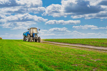 An Agricultural Tractor Drives Along A Field Road. Spring Field
